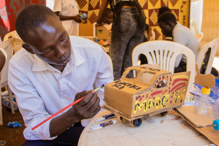 A person paints on a small cardboard vehicle